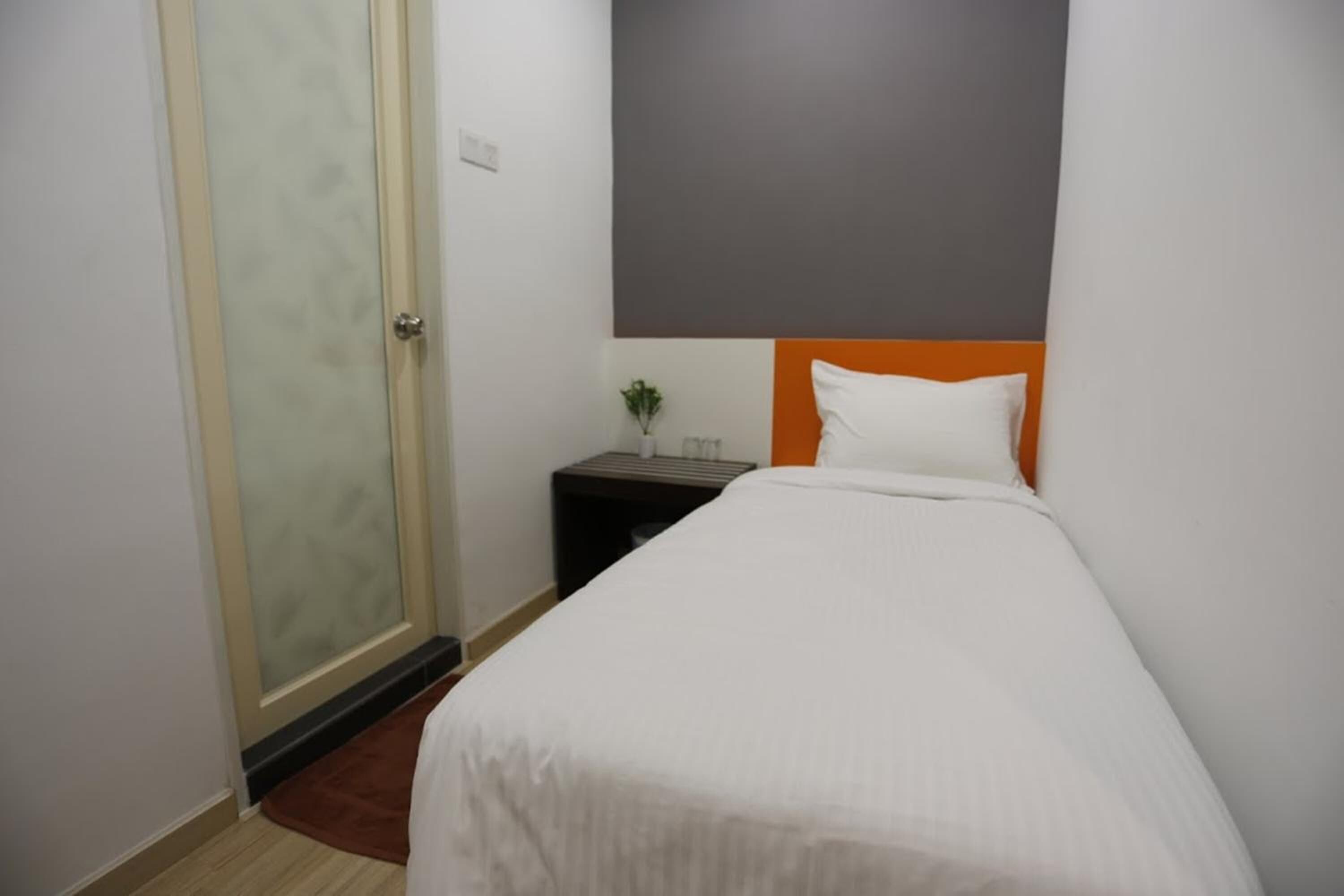 A hotel room with a bed, a nightstand, a small plant, and a door with a frosted glass panel.