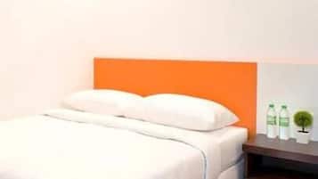 Habitación de hotel con cama, almohadas, mesita de noche con botellas de agua y una pequeña planta en maceta.
