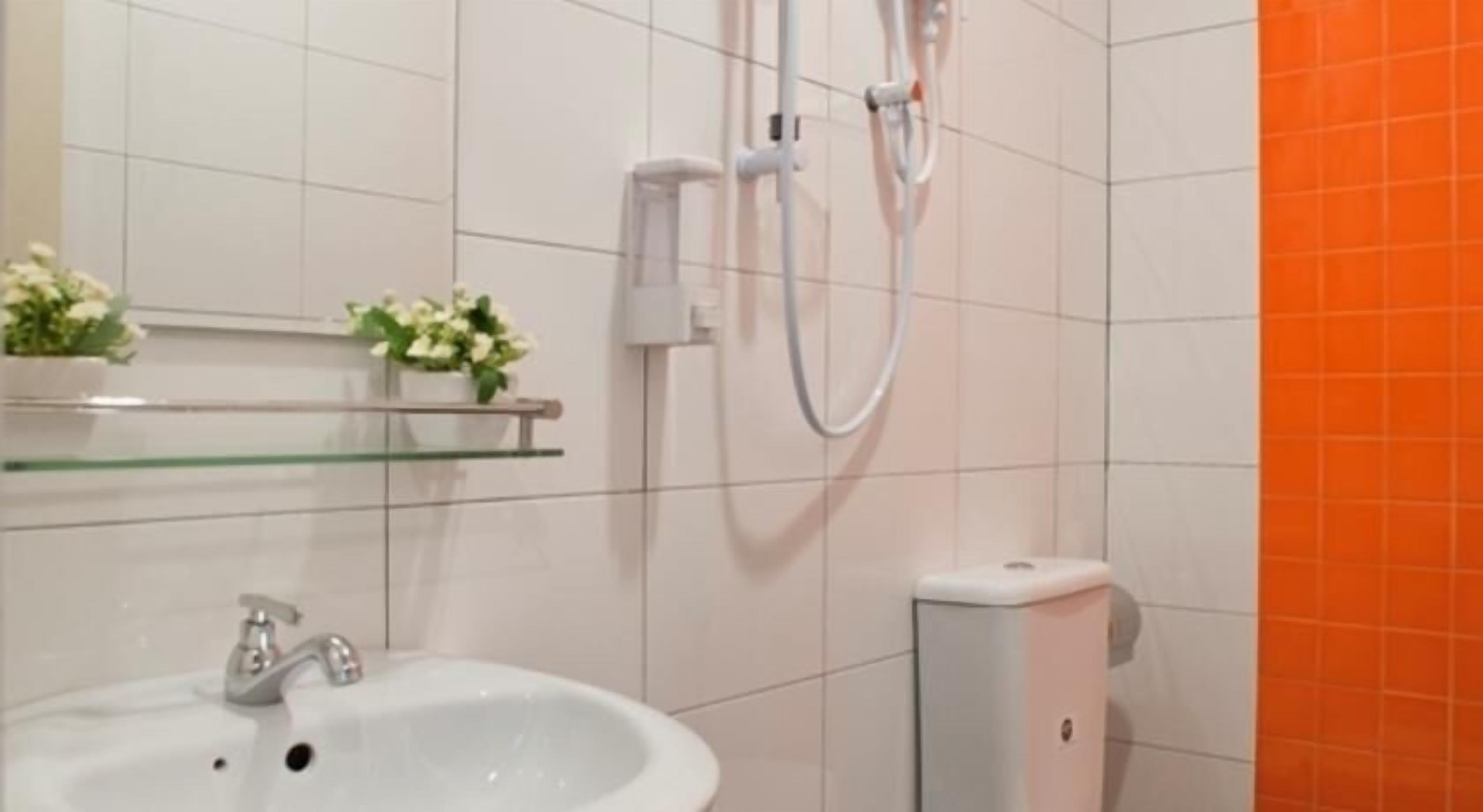 Ein Badezimmer mit einem weißen Waschbecken, einer Glastrennwand mit Blumen, einer weißen Toilette und einer Dusche mit Duschschlauch.