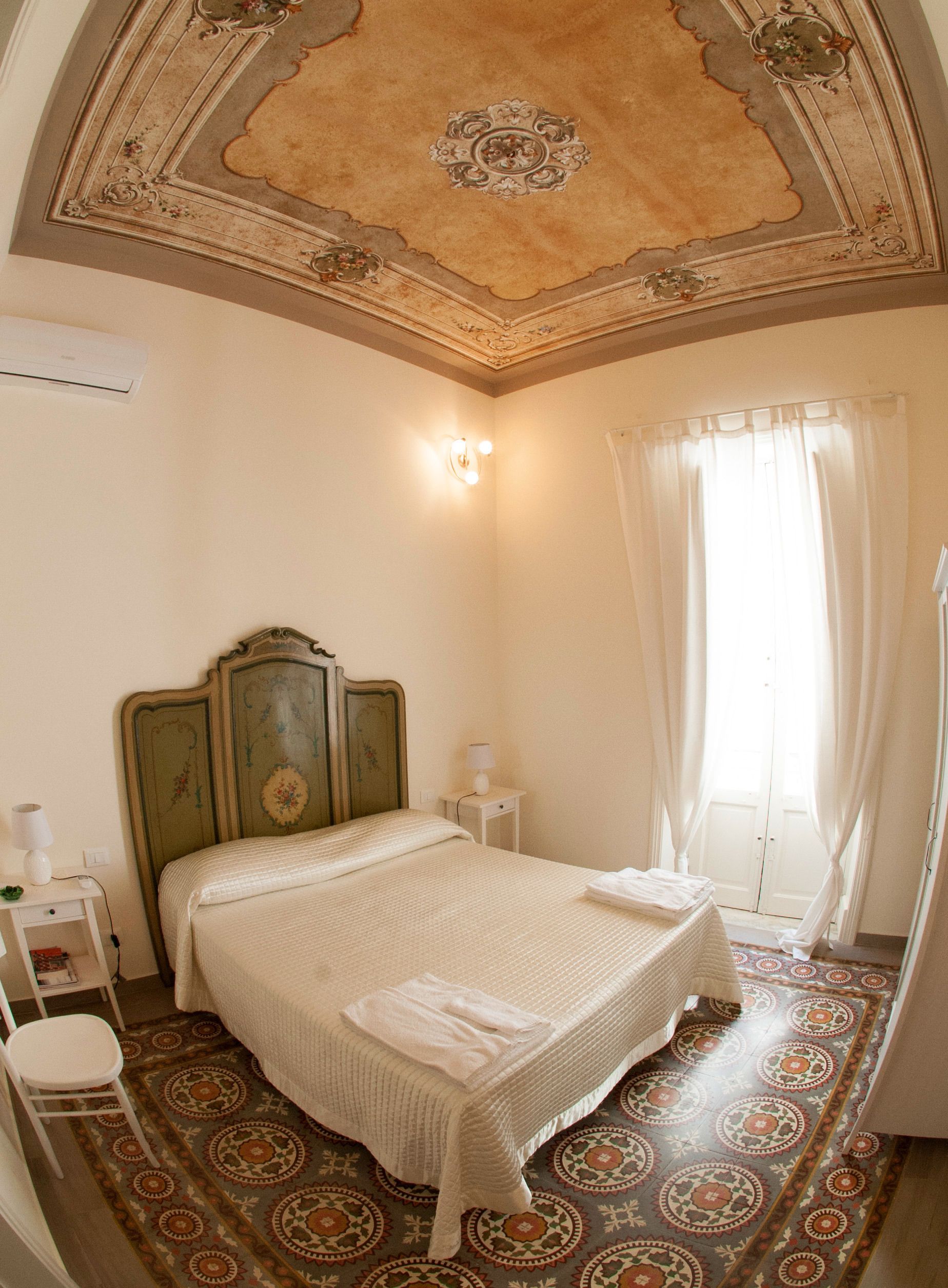 A bedroom with a bed, a nightstand, a lamp, a wall-mounted air conditioner, and a patterned floor.
