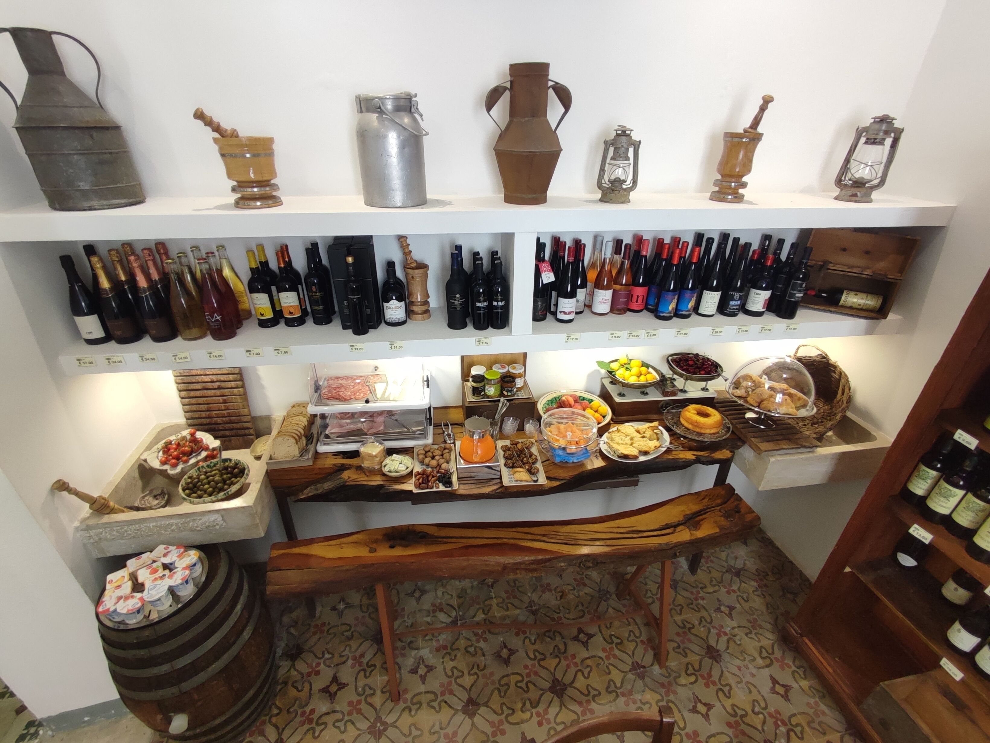A wine cellar with shelves of wine bottles, a wooden counter with food items, and antique kitchenware.