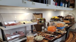 Un bufé con diversos alimentos, entre ellos carnes, quesos y frutas, exhibidos sobre una barra de madera.