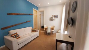 Una sala de estar con un sofá blanco, una pared de acento azul y una zona de comedor con mesa y sillas.