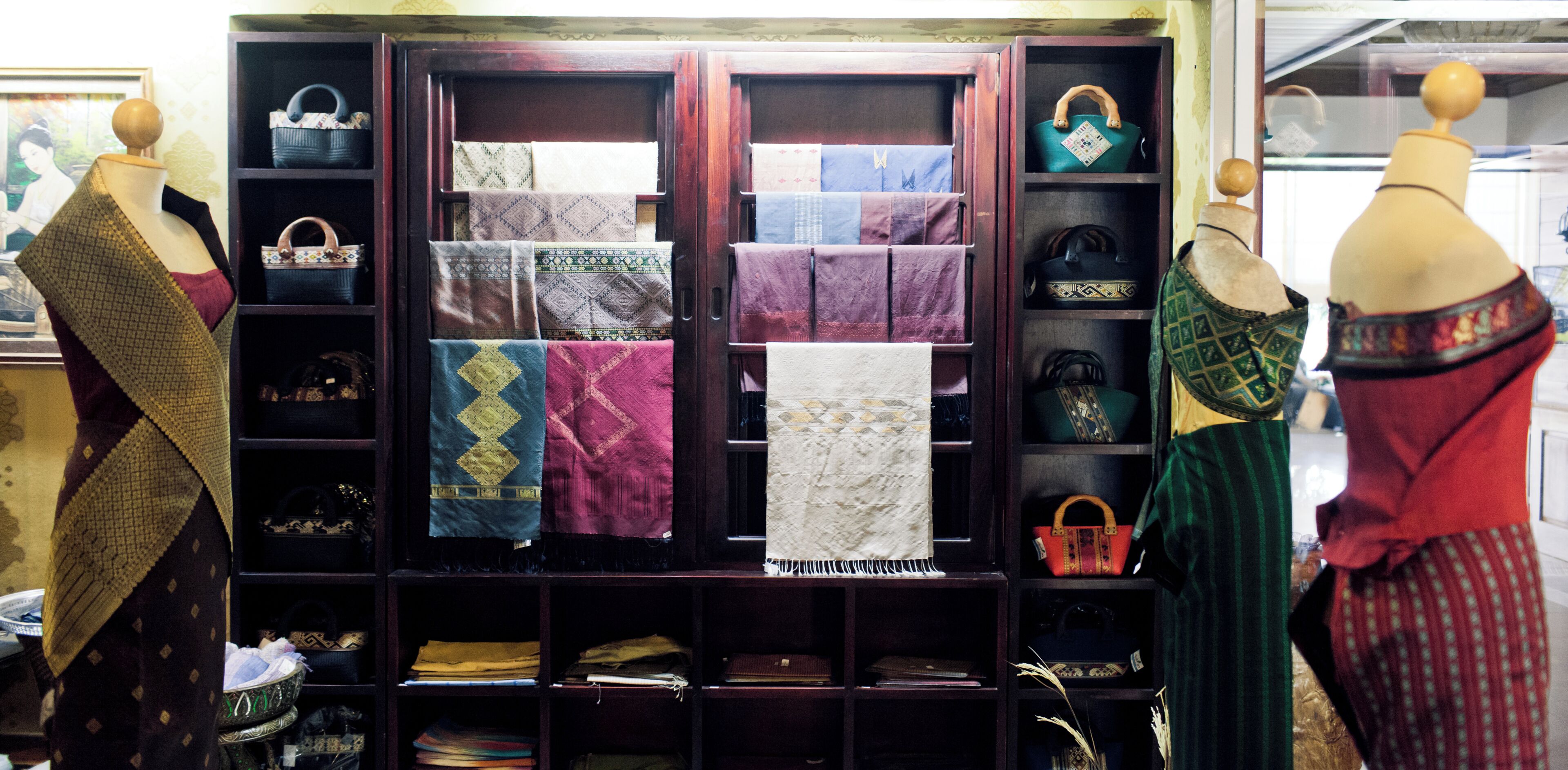 Une exposition de tissus à motifs et de sacs à main, présentés sur des étagères et des mannequins.
