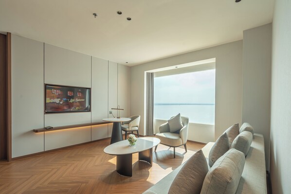 A modern living room with a sofa, a coffee table, a TV, and a large window. - Champasak Grand Hotel (Pakse)