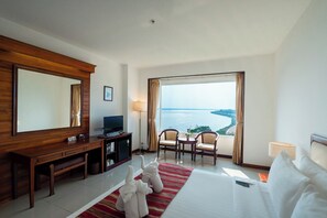 A hotel room with a large bed, a desk with a TV, two chairs, a view of the sea, and a large mirror. - Champasak Grand Hotel (Pakse)