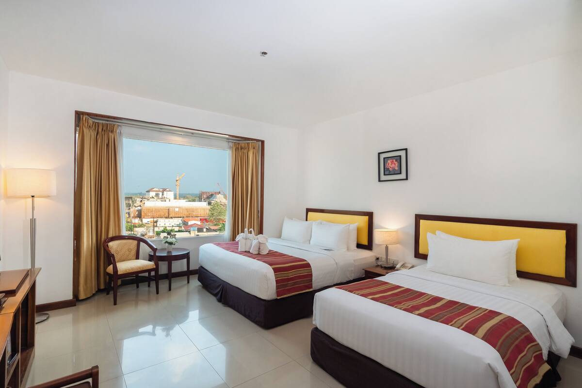 A hotel room with two beds, a chair, a desk, and a window with curtains.