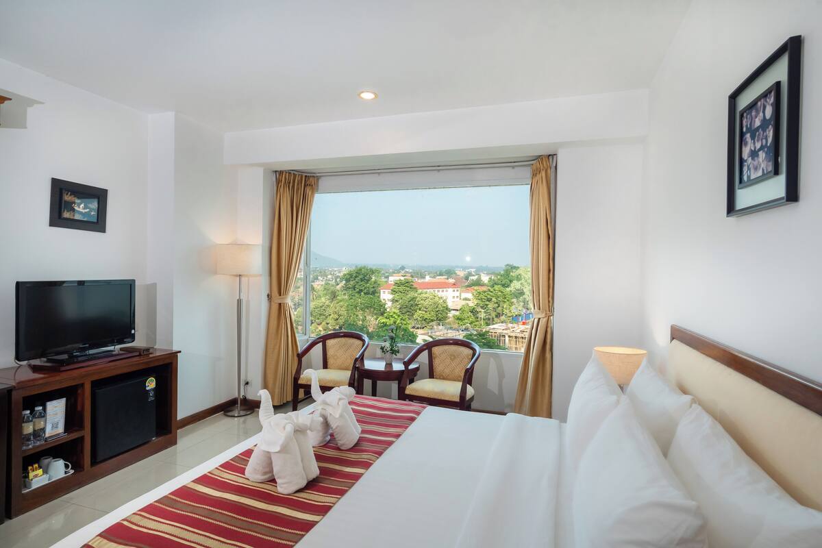 A hotel room with a bed, a TV, a desk, and a view of the city.