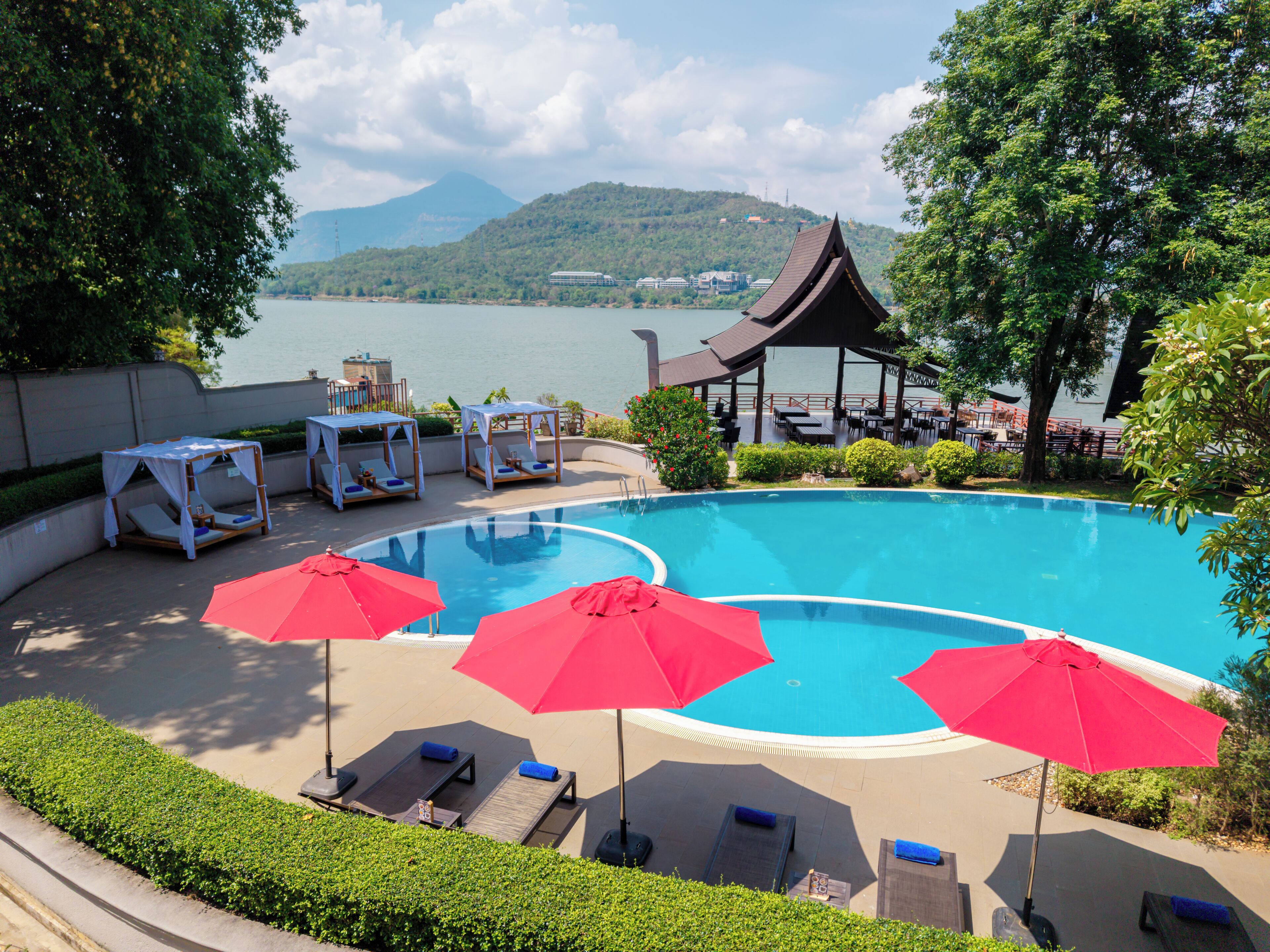 A swimming pool with lounge chairs and umbrellas, surrounded by greenery and a view of a lake and mountains.