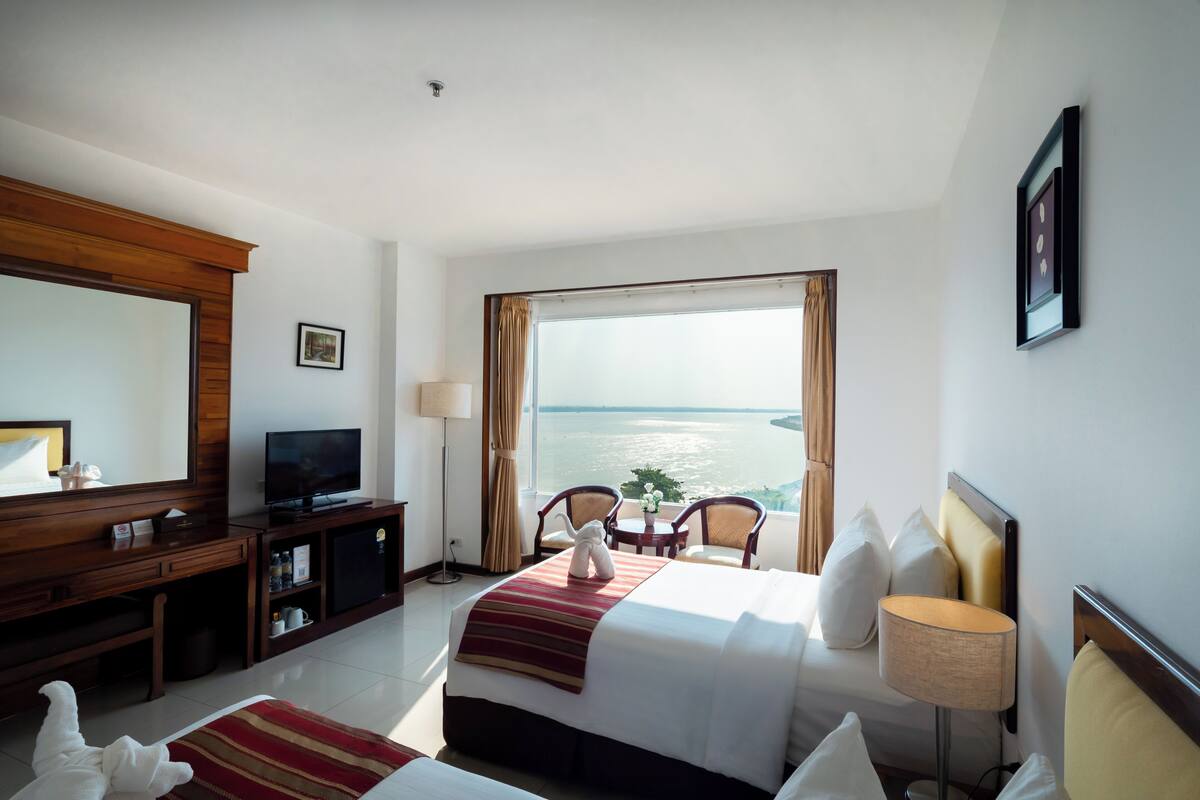 A hotel room with a bed, television, desk, and a view of the sea.