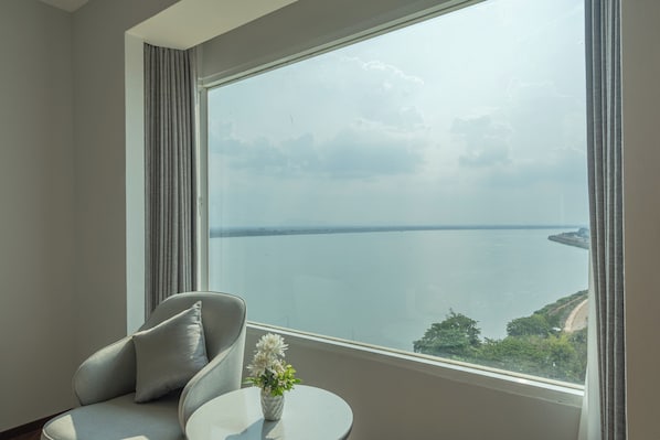 A room with a large window, a sofa, a small table, and a vase of flowers. - Champasak Grand Hotel (Pakse)
