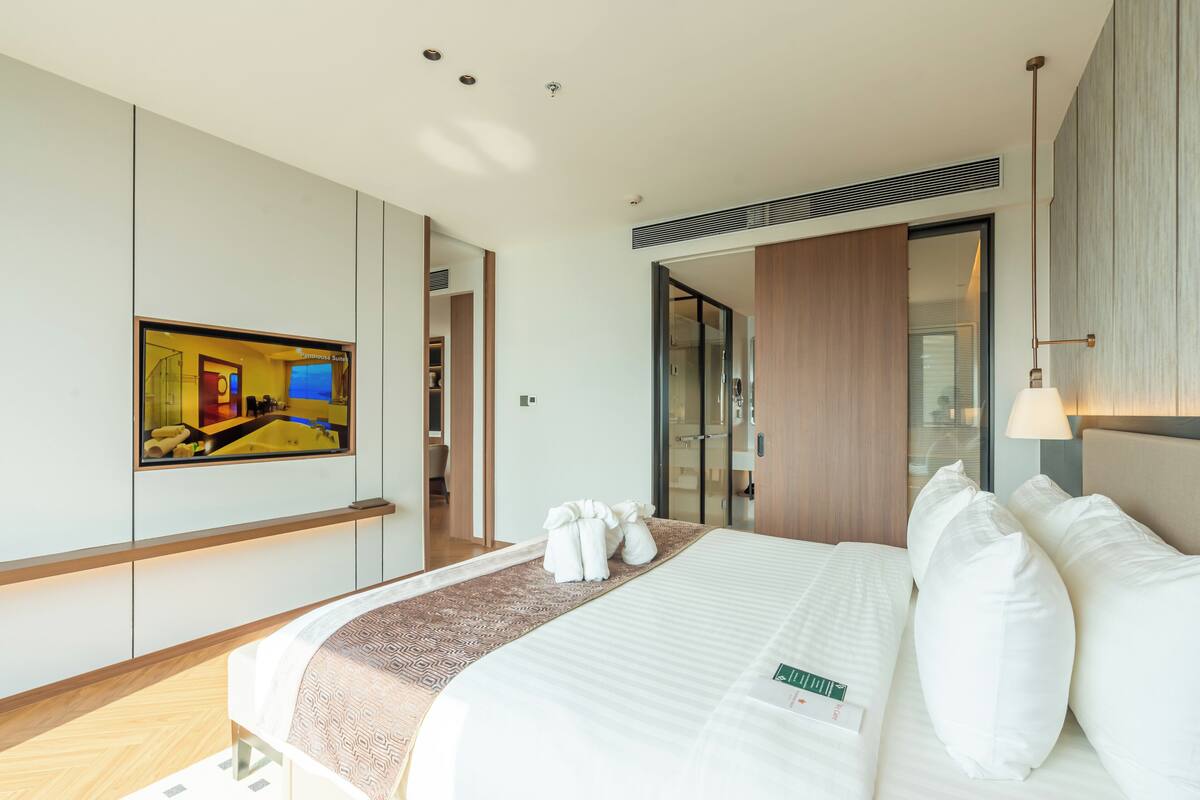 A hotel room with a bed, a large mirror, a painting, and a view of the bathroom.