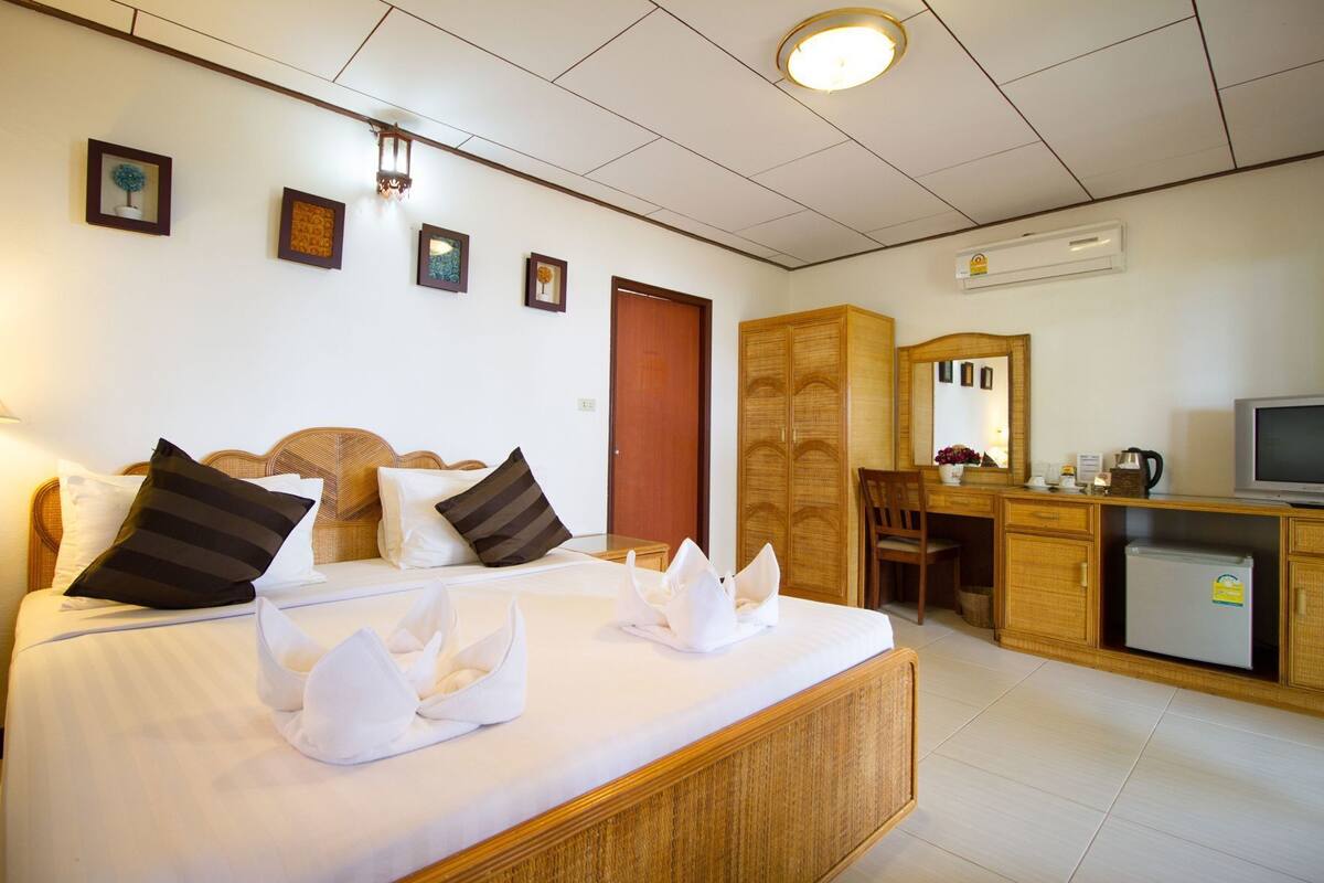 A hotel room with a bed, bedside table, desk, chair, television, and an air conditioning unit.
