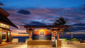 A sunset view from a covered outdoor seating area with a sign reading "SUNSET BAR".