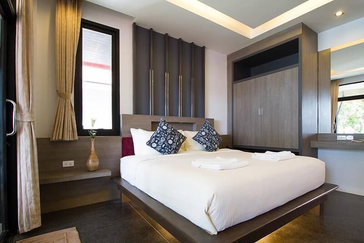 A modern hotel room with a large bed, a bedside table, a wardrobe, and a window with curtains.