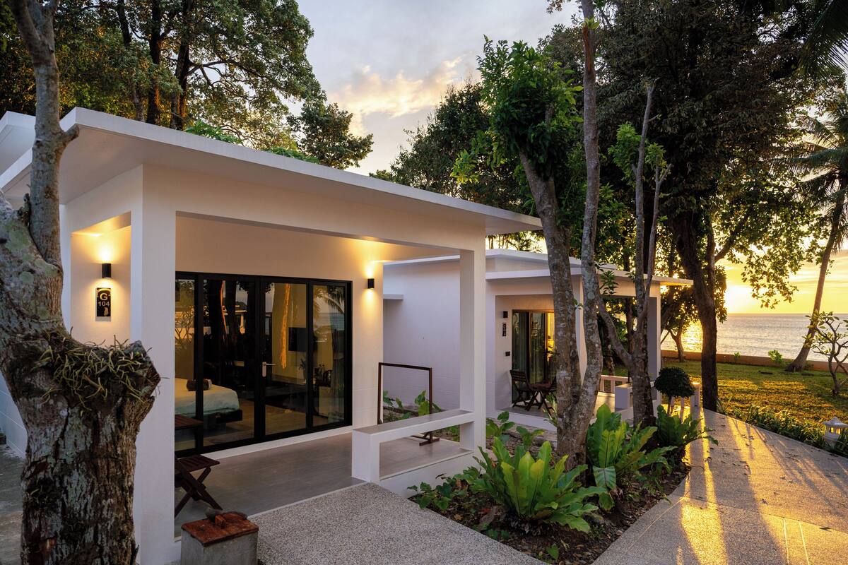 A modern house with a glass facade, outdoor seating, and a view of the sea.