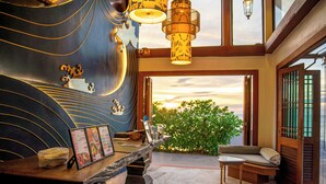 A modern interior with a wooden reception desk, a seating area with a cushioned bench, and a view of the sunset through large windows. - Koh Chang Grandview Resort (Ko Chang)