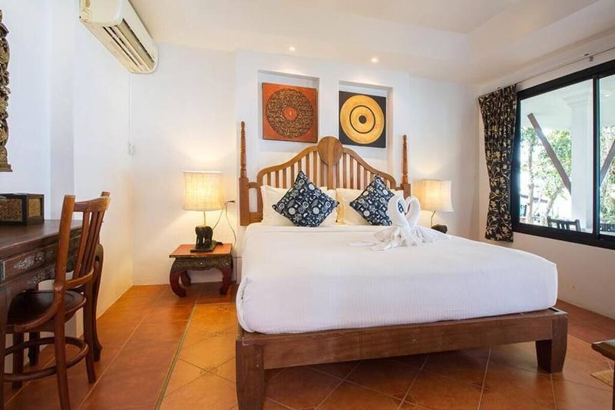 A bedroom with a wooden bed, two wall-mounted lamps, a chair, and a window with curtains.