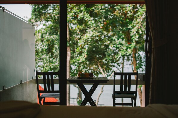 A balcony with a table and two chairs, overlooking a lush green area.