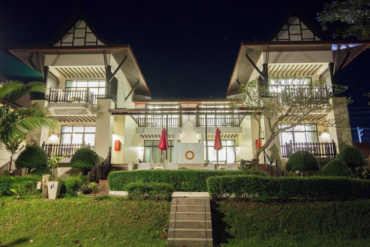 A two-story hotel with a balcony on each floor, a covered entrance, and a well-maintained garden.