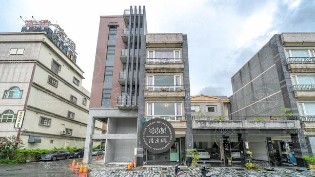 A modern building with a prominent circular logo, multiple balconies, and a parking area with motorcycles. - Discovery B&B (Hualien City)