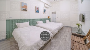 A hotel room with two beds, a wooden floor, a green headboard, a small table with a vase, and a television on the wall. - Discovery B&B (Hualien City)