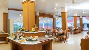 A spacious dining area with multiple tables and chairs, a buffet counter with various food items, and large windows offering a view of the surrounding landscape. - The Fog Munnar Resorts & Spa (Devikolam)
