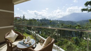 A balcony with wicker furniture, a glass table, and a scenic view of a mountainous landscape. - The Fog Munnar Resorts & Spa (Devikolam)