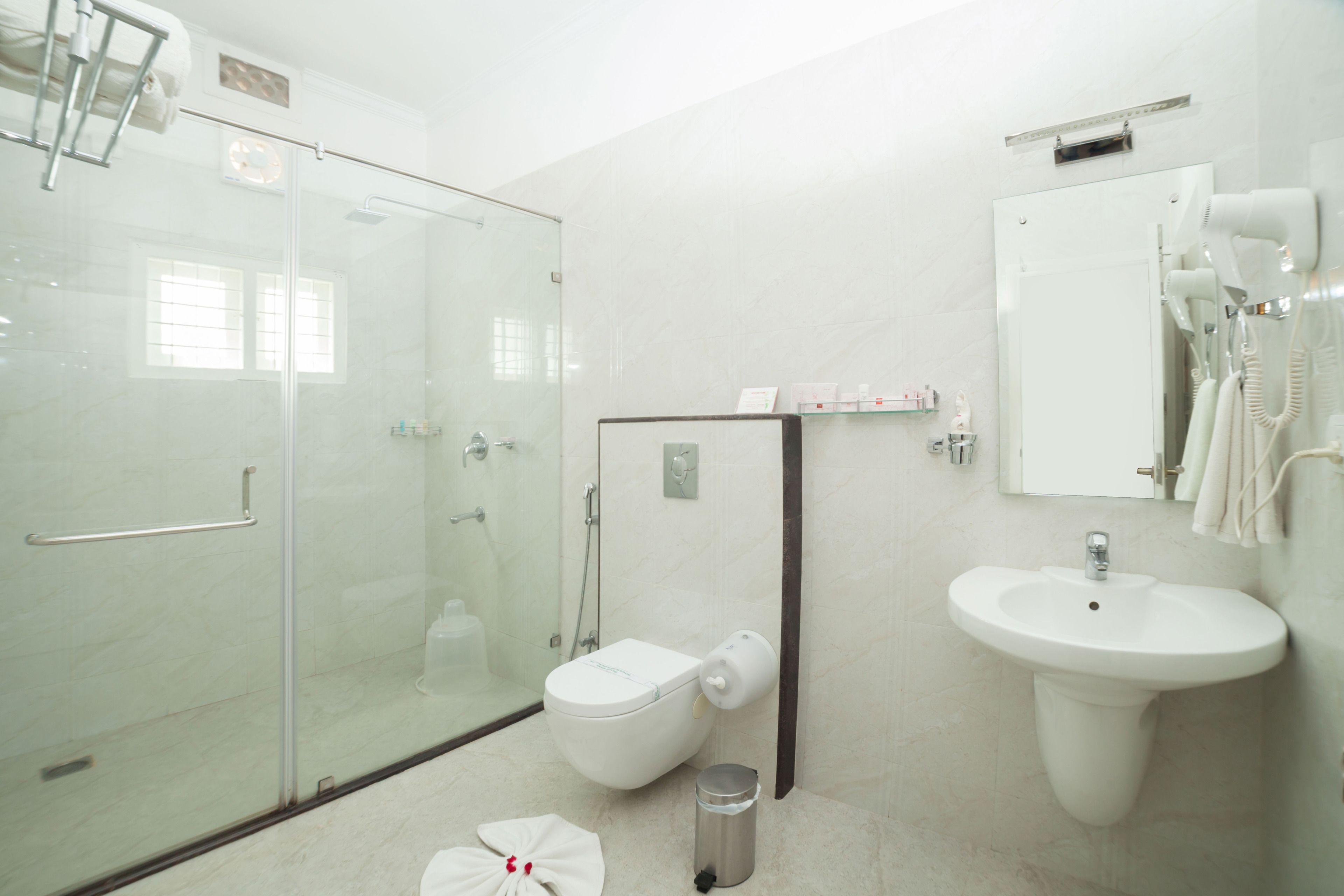 A modern bathroom with a glass shower enclosure, a toilet, a sink, and a hairdryer mounted on the wall.