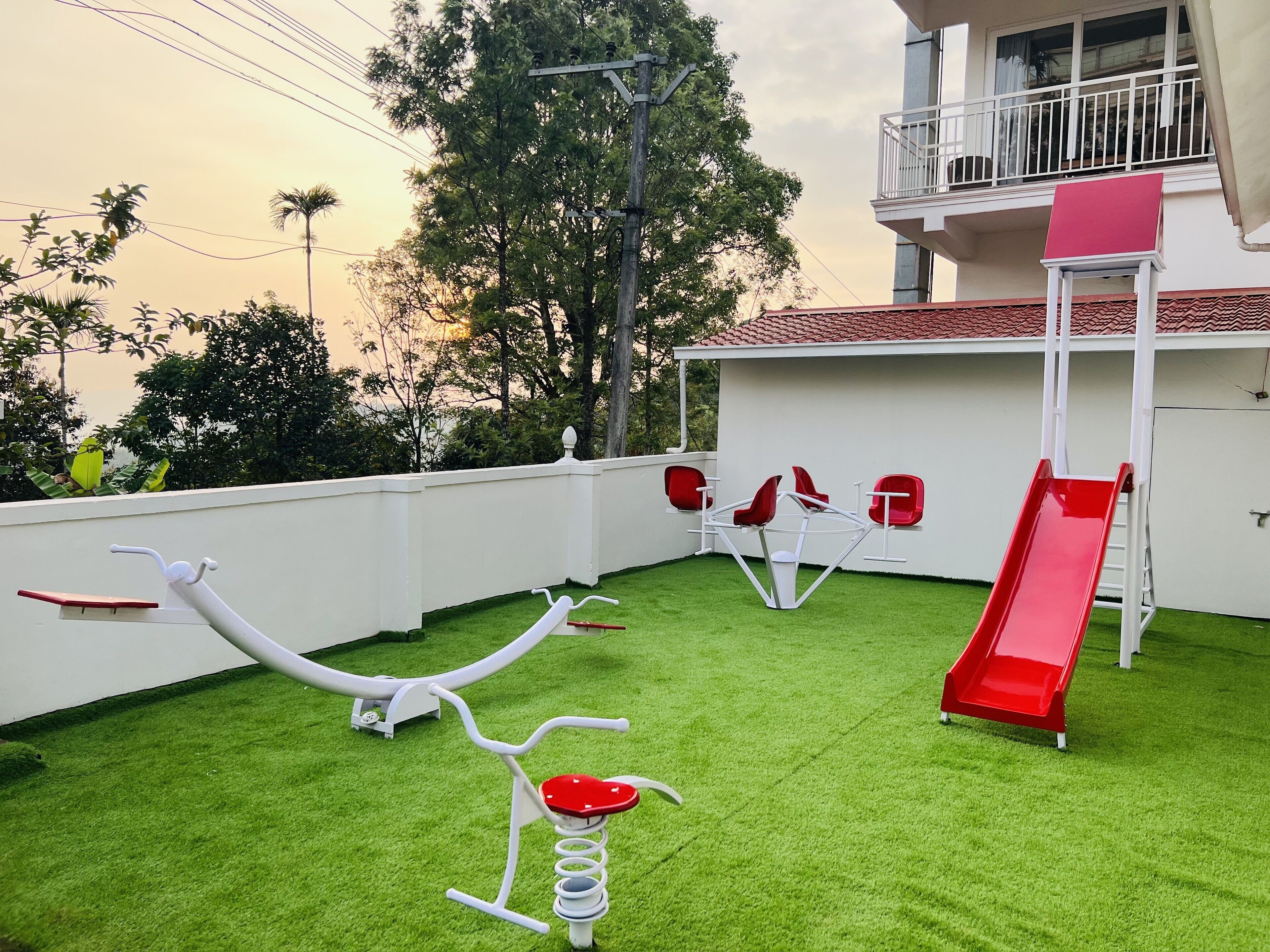 A children's play area with a slide, swings, and a merry-go-round on artificial grass.
