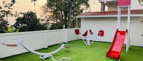 A children's play area with a slide, swings, and a merry-go-round on artificial grass.