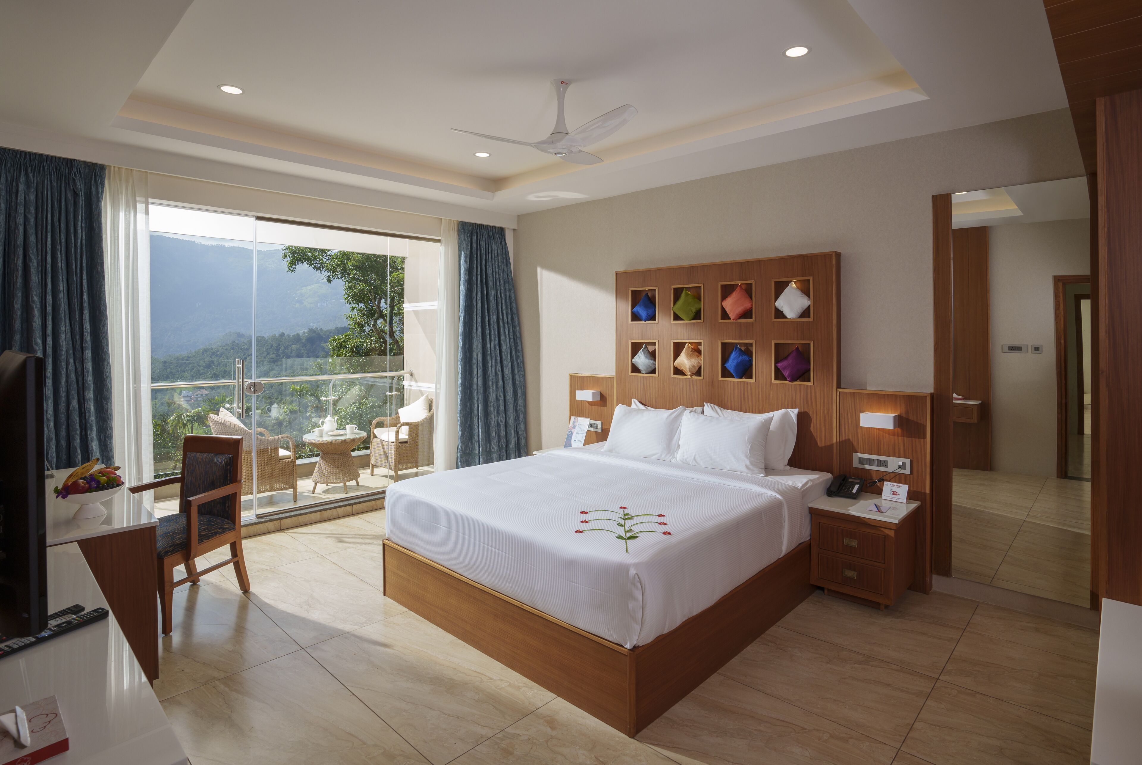 A spacious hotel room with a large bed, a balcony with a view, a desk with a chair, and a TV.