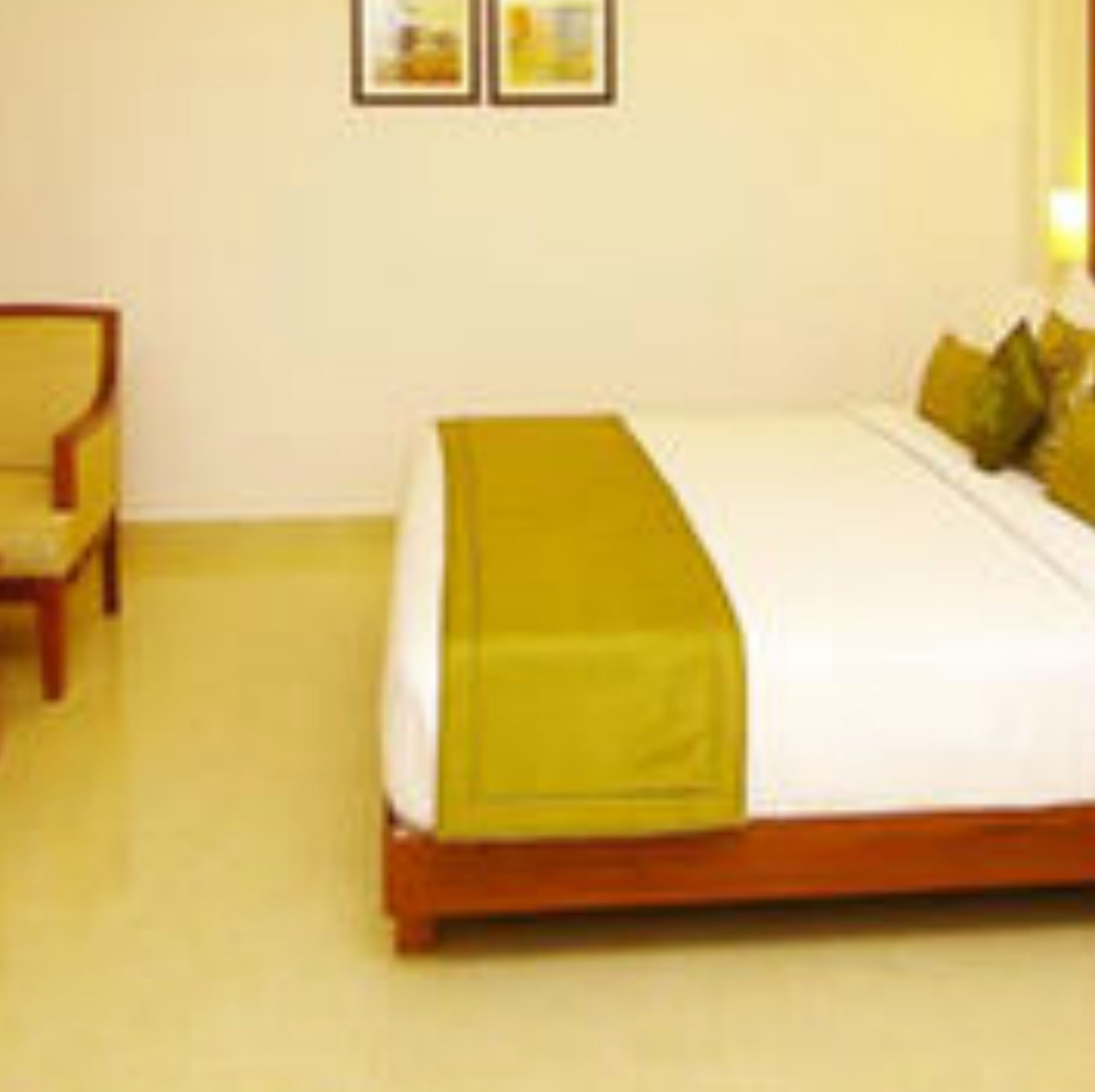 A hotel room with a bed, a chair, and two framed pictures on the wall.