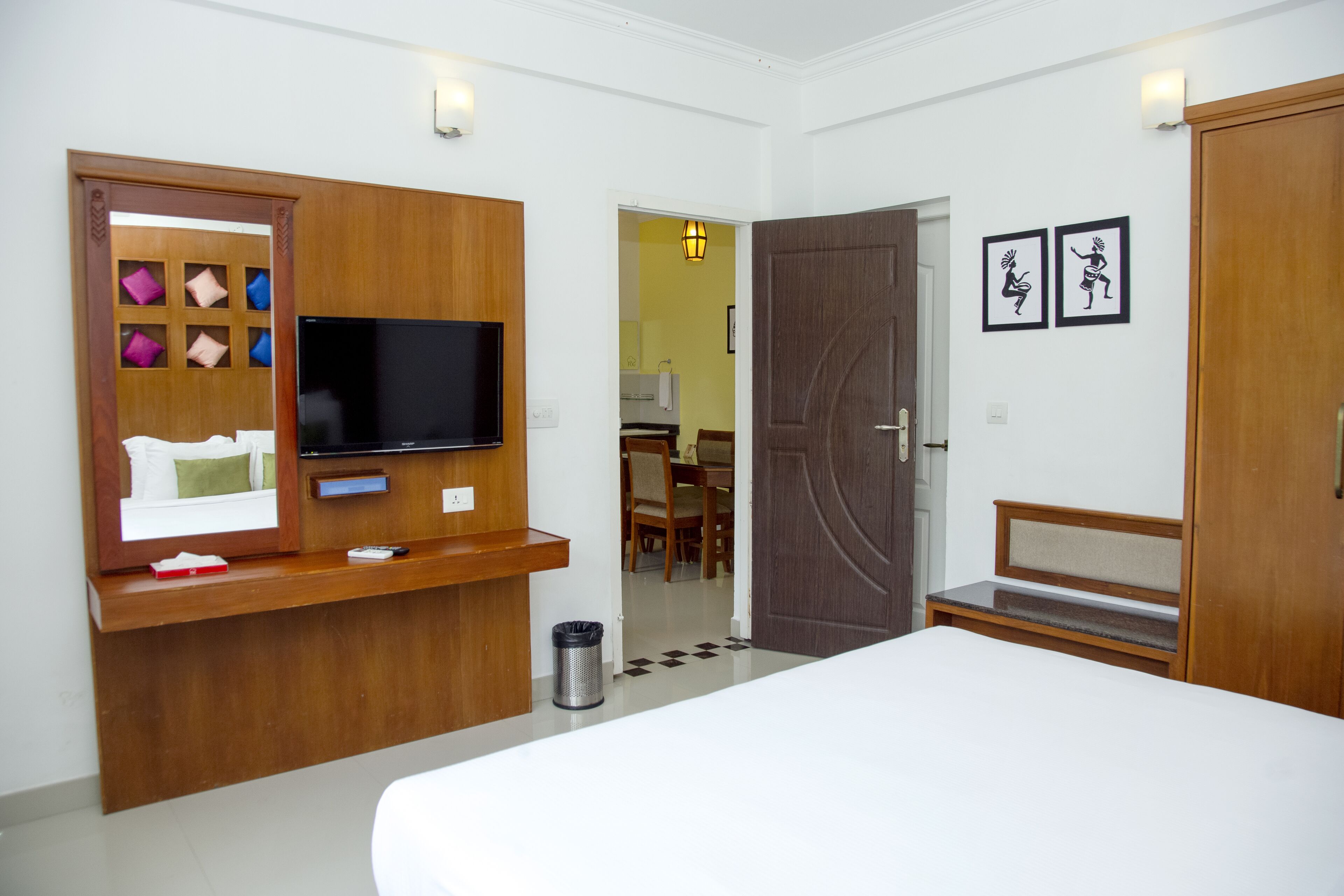 A hotel room with a bed, a TV, a wooden desk, a chair, and a door leading to another room.