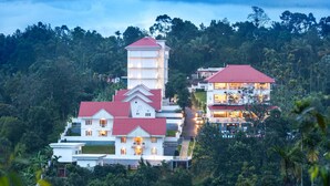 A multi-story building with a red roof, surrounded by lush greenery and trees. - The Fog Munnar Resorts & Spa (Devikolam)