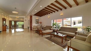 A spacious living area with a high ceiling, a fireplace, and large windows offering a view of the outdoors. - The Fog Munnar Resorts & Spa (Devikolam)