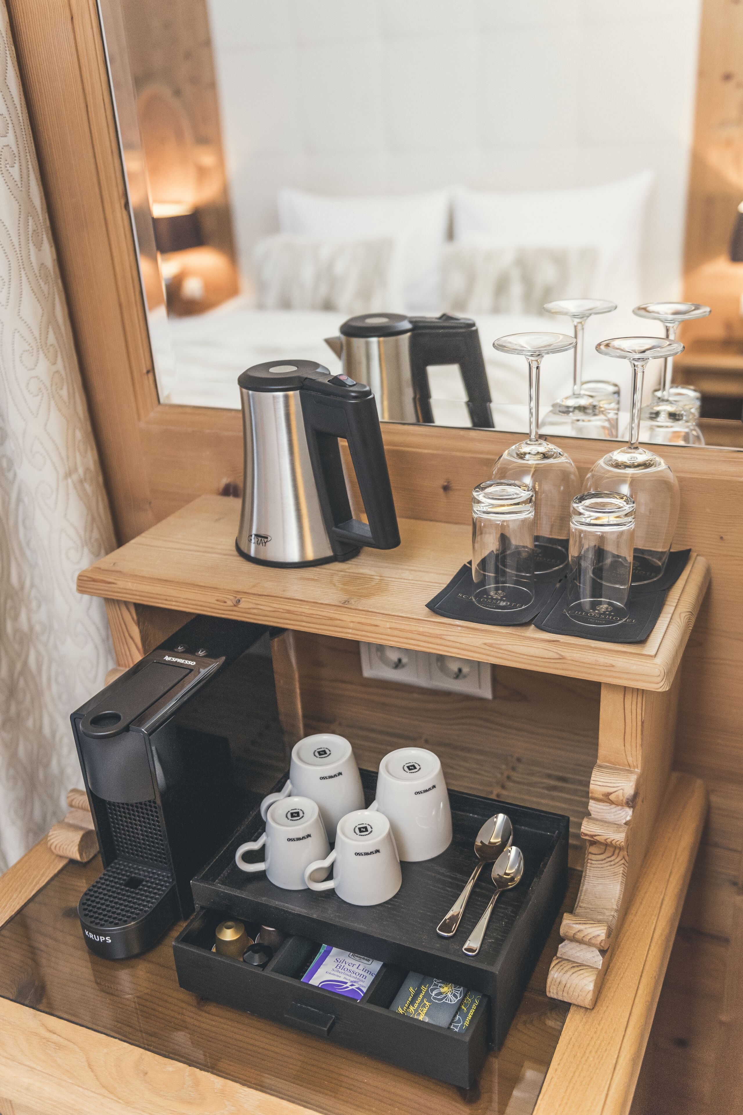A hotel room with a wooden side table holding a coffee maker, cups, and a tray with utensils.