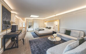 A modern hotel room with a large bed, a sofa, a desk, and a small table with fruit.