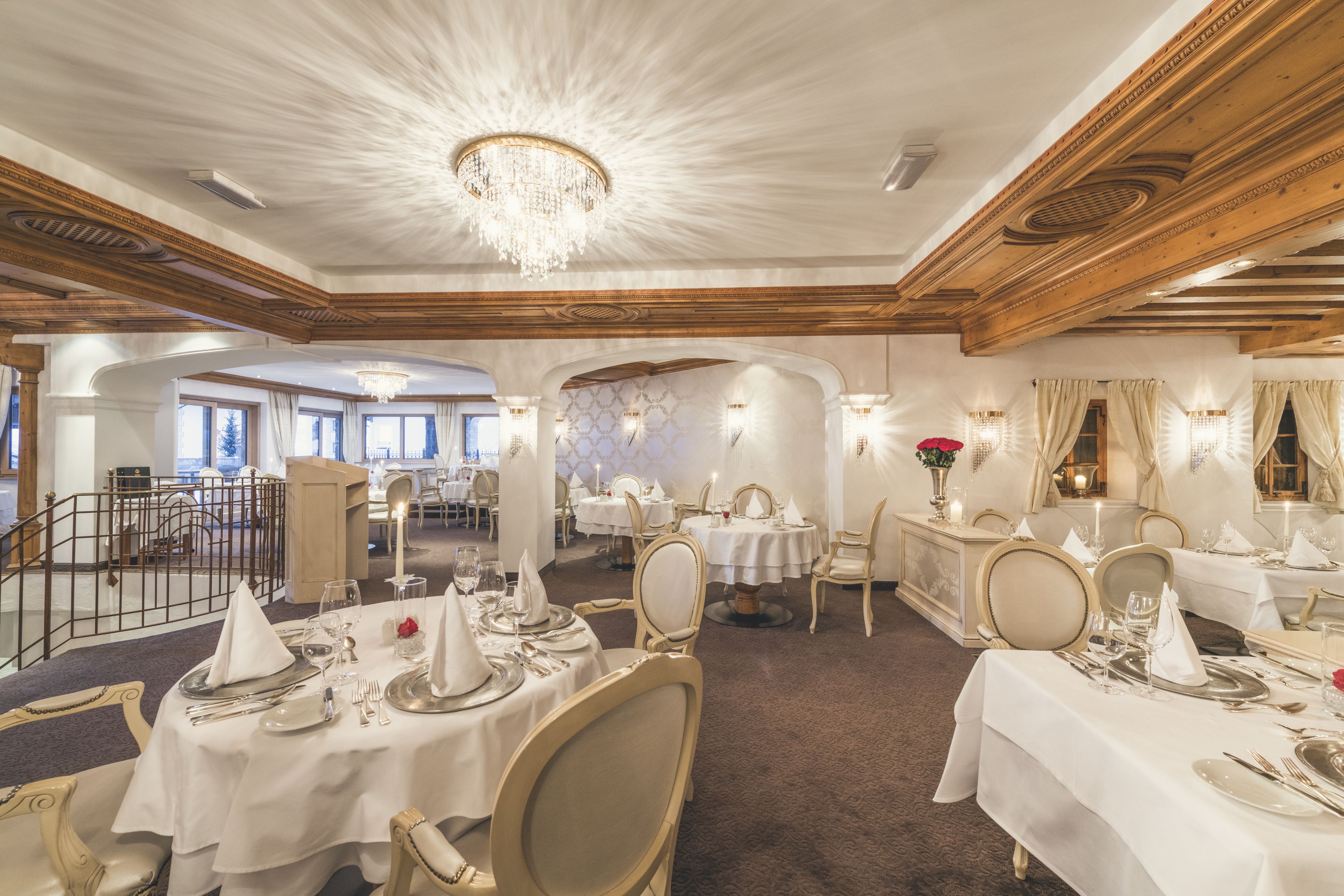Une salle à manger élégante, avec des tables rondes, des nappes blanches et des éléments décoratifs dorés.