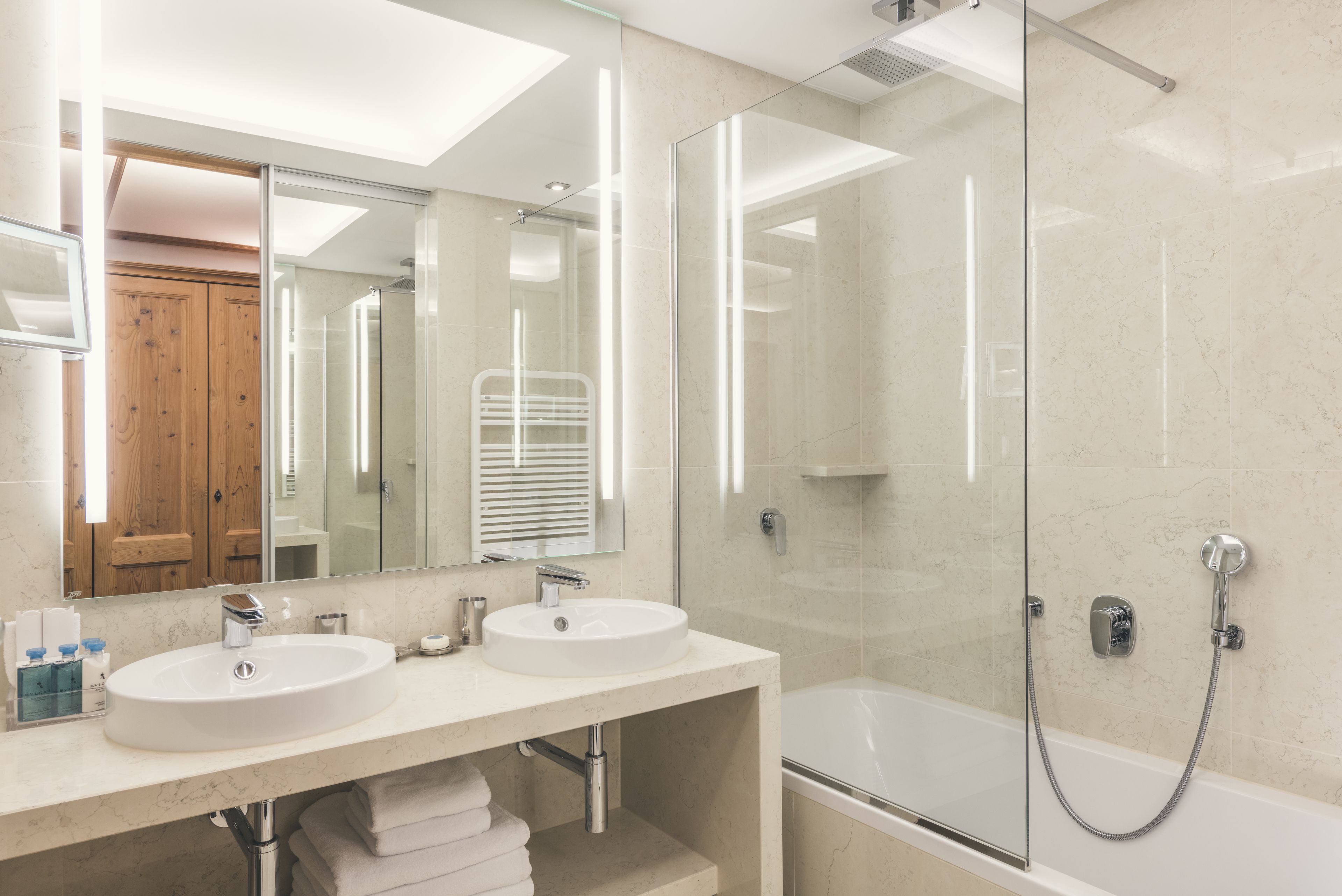 Un baño moderno con dos lavamanos, un espejo grande y una ducha con cerramiento de vidrio.