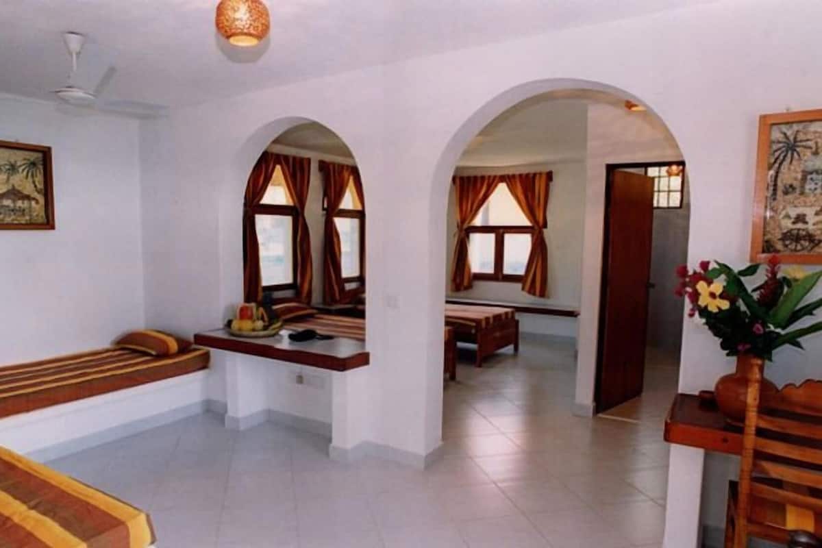 A room with a bench, a table, and a chair. There are two windows with curtains.