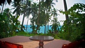 A round wooden table with a metal frame, surrounded by lush greenery and palm trees, overlooking a beach. - Eva Lanka Hotel (Morakatiyara)
