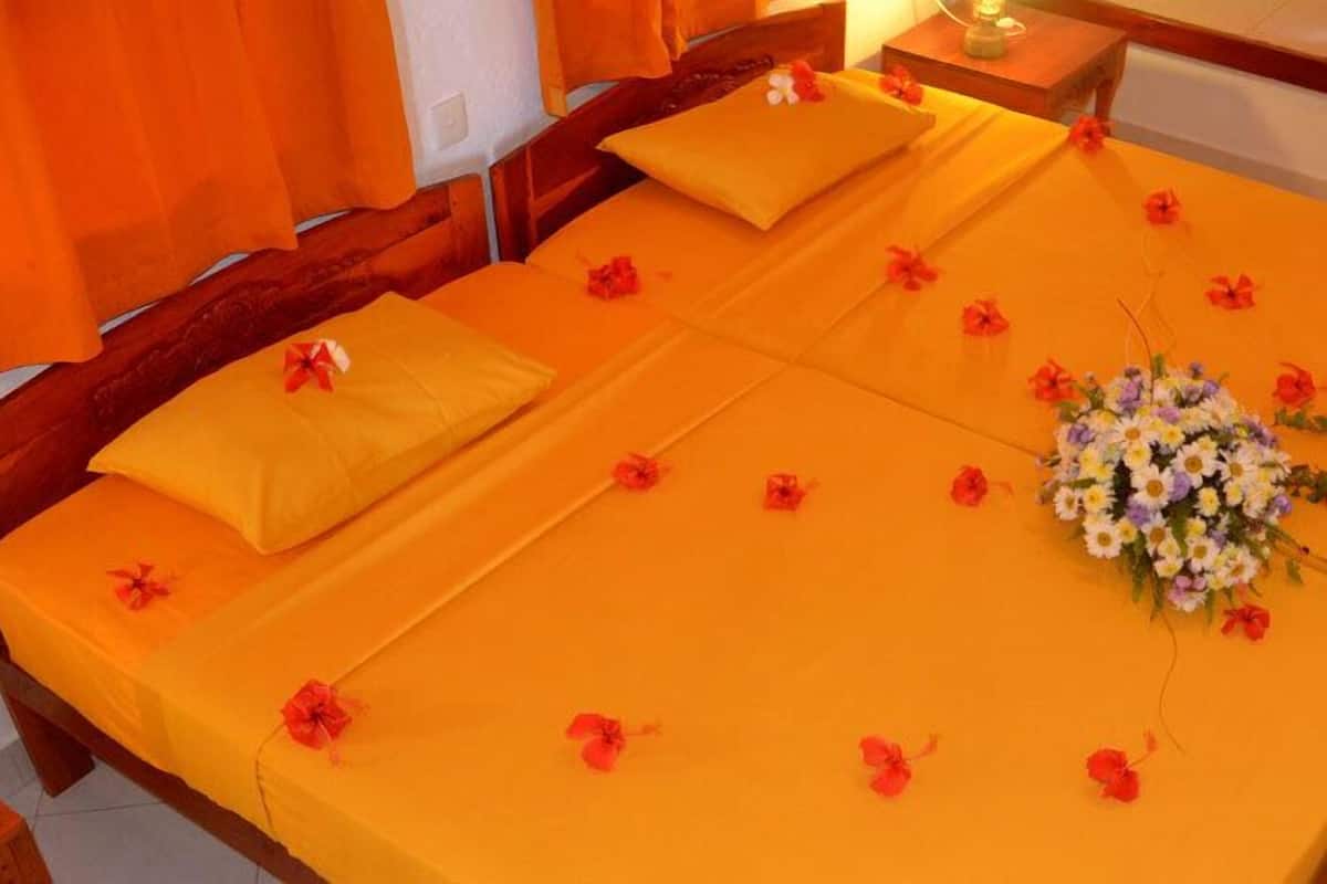 A double bed with orange bedding and pillows, a floral centerpiece, and scattered red flowers.