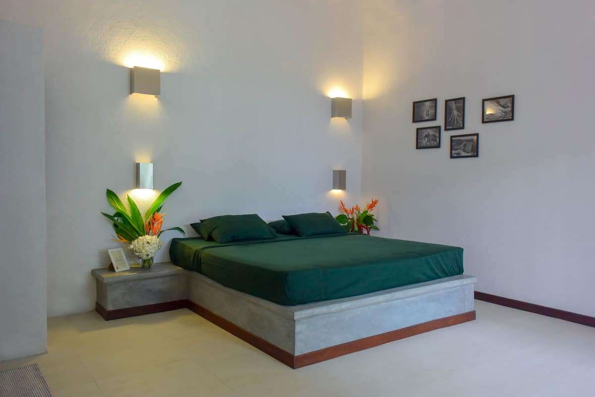 A modern bedroom with a large bed, bedside tables, wall-mounted lights, and framed pictures.