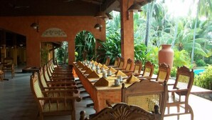 A long dining table with chairs, surrounded by lush greenery and a tiled floor. - Eva Lanka Hotel (Morakatiyara)
