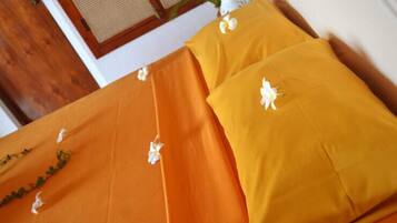 Un lit avec une couvre-lit orange et des oreillers, décoré de fleurs blanches.