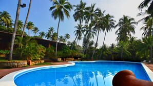 A swimming pool surrounded by palm trees and a building with a curved roof. - Eva Lanka Hotel (Morakatiyara)