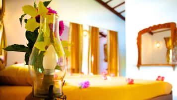 Una habitación con una cama cubierta de sábanas amarillas, un florero con flores y un espejo en la pared.