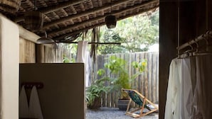 A small, rustic room with a thatched roof, wooden benches, and a view of a garden. - Casas da Vila (Porto Seguro)