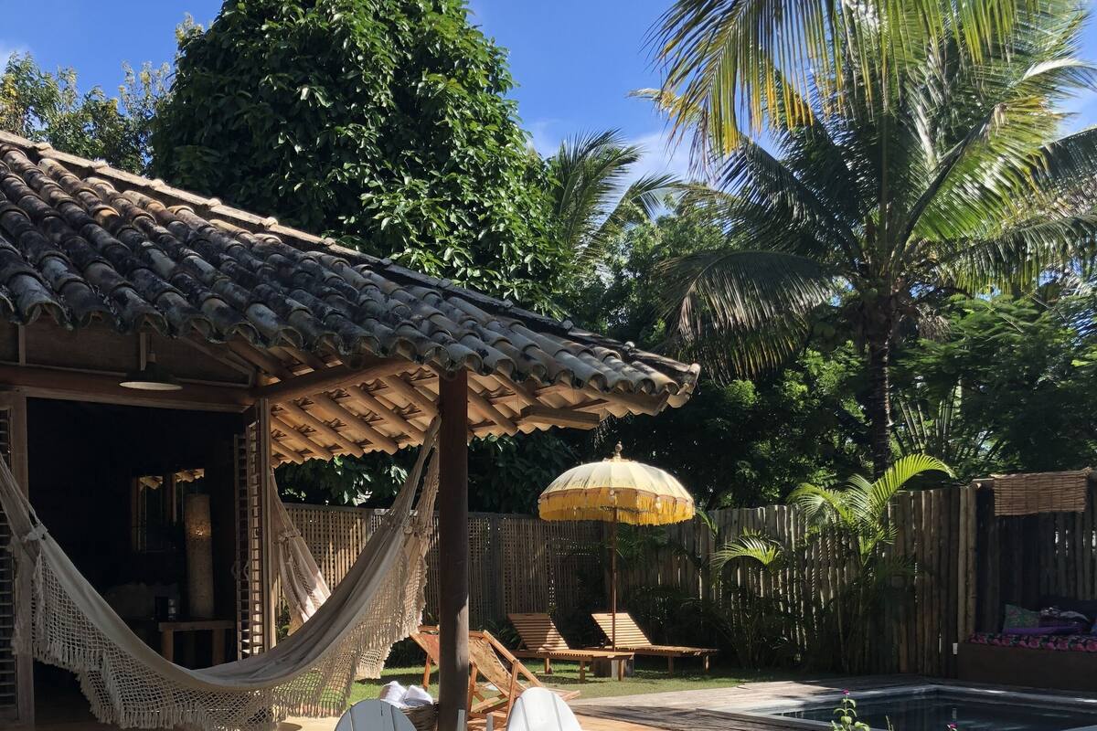 Eine Terrasse mit einer Hängematte, weißen Stühlen, einem Holztisch und einem kleinen Pool.